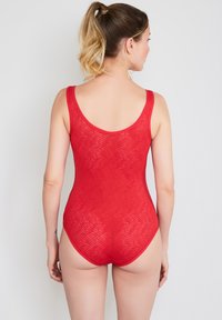 Punainen uimapuku aaltoilevalla, teksturoidulla kuviolla, pyöreällä selkäosalla ja leveillä olkaimilla. Valmistettu joustavasta kankaasta, joka tarjoaa tiukan istuvuuden.