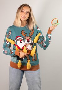 Hellblauer gestrickter Pullover mit einem Weihnachtsdesign, das Santa und ein Rentier zeigt, akzentuiert mit gelben Formen, kombiniert mit lässigen Jeans.