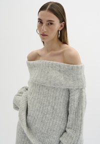 Pulover gri cu umeri descoperiți, cu textură cu nervuri, mâneci lungi și croială lejeră, realizat dintr-un material moale și ușor.