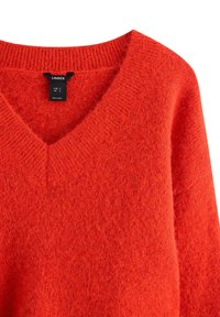 Svetr s výstřihem do V a dlouhými rukávy v jasně červené barvě, s měkkou pletenou strukturou a žebrovaným límcem. Uvnitř viditelná značka značky.