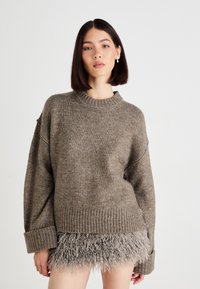 Brun strikkegenser med ribbede mansjetter og hem, kombinert med en grå fluffy miniskjørt, som har en teksturert kontrast nederst.