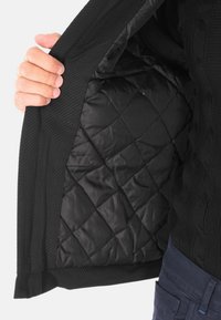 Interno della giacca nera con un motivo trapuntato in tessuto morbido. Il materiale esterno presenta un design intrecciato testurizzato.