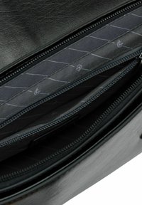 Interno di una borsa in pelle nera caratterizzato da numerosi scomparti con zip, foderati in tessuto grigio, con motivi di cuciture diagonali e zip rinforzate.