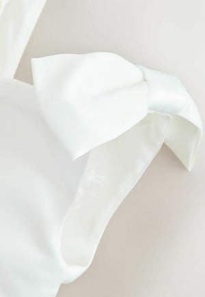 Bela satenasta pentlja pritrjena na gladek beli trak iz tkanine na nevtralnem ozadju.