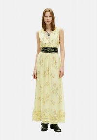 Maksiklases kleita no maigas dzeltenas auduma ar ziedu rakstiem. Tai ir piegulošs melns jostas ar naglām, slāņveida apakšmala un īsas piedurknes.