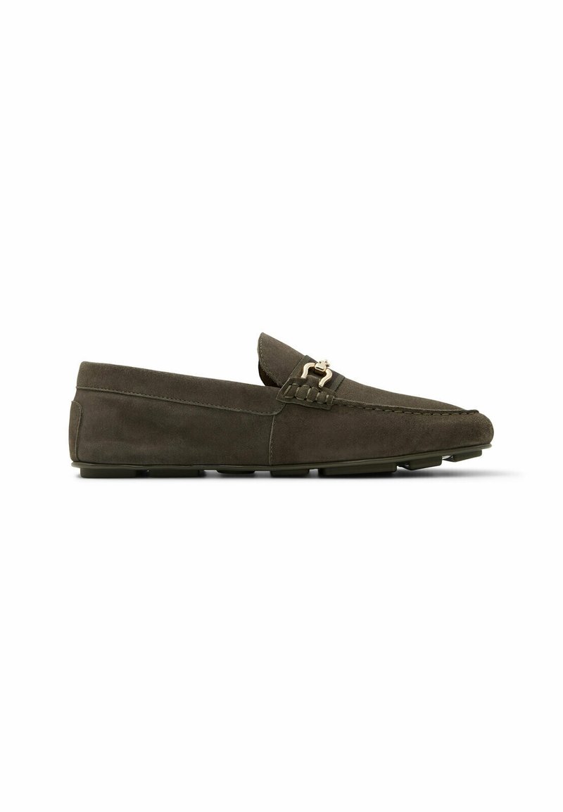 Mocassin en daim brun foncé avec un détail de boucle en métal sur le devant et une semelle extérieure cloutée en caoutchouc pour une meilleure adhérence.