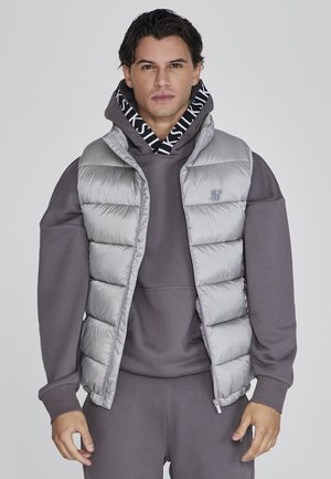 Chaleco gris acolchado sobre una sudadera con capucha gris a juego, con frente con cremallera y un diseño acolchado que incluye un logo en el pecho.