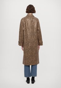 Leopard-print waterproof trench coat in brown and black, featuring a classic collar and long sleeves. Exposed stitching detail on back.
