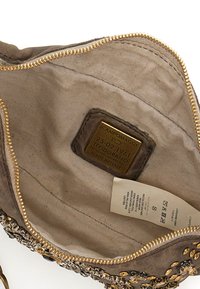 Interno di una borsa da donna in pelle marrone con una zip, dotato di fodera in tessuto e un'etichetta in metallo. L'hardware decorativo include gemme.