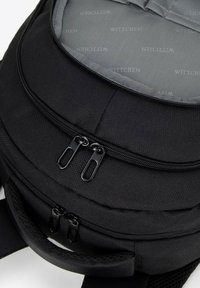 Mochila negra con dos compartimentos con cremallera, hecha de un tejido duradero, con un forro interior suave que presenta un patrón de logotipo repetido y correas acolchadas.