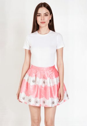 Top blanco de manga corta combinado con una falda floral rosa plisada que presenta grandes flores rosas y pequeños acentos marrones. Textura suave.