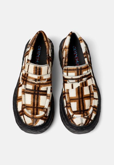 Een paar instap schoenen met een bruin en wit geruit bontpatroon en dikke zwarte zolen, van bovenaf gezien op een witte achtergrond.