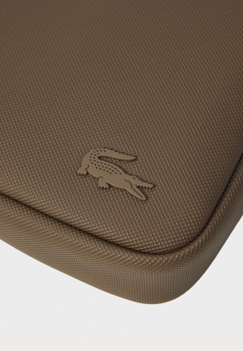 Manchon pour ordinateur portable en cuir texturé marron avec des bords arrondis ; présente un logo de crocodile en relief de couleur assortie pour une marque discrète.