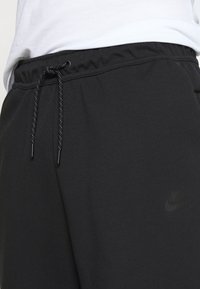 Mustat verkkarit, jotka on valmistettu pehmeästä kankaasta, jossa on elastinen vyötärö, nauhakiristys ja huomaamaton Nike-logo sivulla.