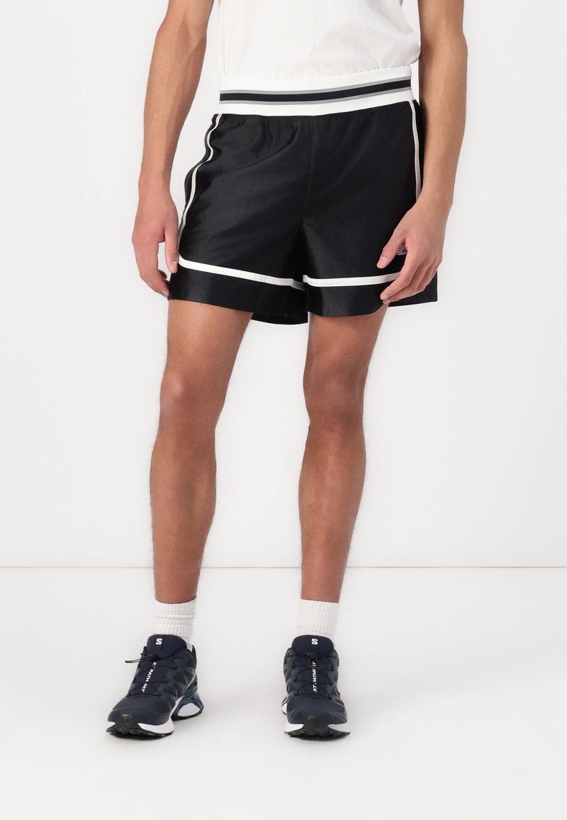 Shorts de sport noirs avec une bande blanche contrastante le long de l'ourlet et de la taille, fabriqués dans un matériau lisse et léger.