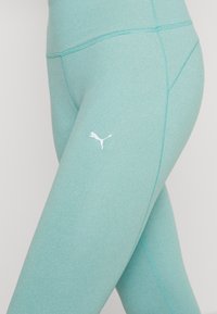 Ljus teal leggings i sträckbart material, med en vit Puma-logotyp och en slät, sömlös design med kurviga sömmar.