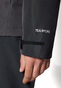 Manga de jaqueta impermeável preta TEXAPORE com fecho de velcro. Tecido suave e texturizado visível, evidenciando um design elegante e qualidade durável.