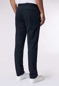 Temno modre chinos hlače s slim fit krojem, narejene iz bombaža z gladko teksturo. Imajo zadnje žepe in subtilne šive.