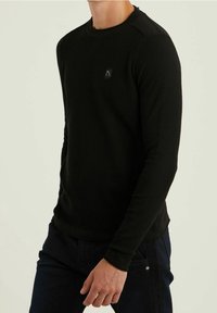 Černá mikina s dlouhým rukávem, zdobená texturovaným pleteným vzorem, kulatým výstřihem a malým logem na hrudi. Hladká látka s přiléhavým střihem.