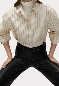 Beige randig skjorta med långa ärmar och krage, i kombination med svarta läderbyxor, som har en framficka och knappstängning.
