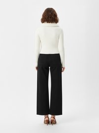 Biały sweter prążkowany z wysokim kołnierzem, w zestawieniu z czarnymi spodniami o szerokich nogawkach z wysokim stanem i brązowymi sandałami na obcasie.