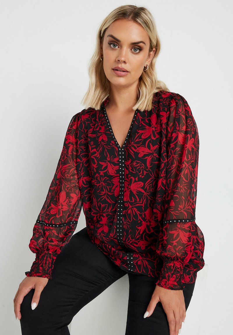 Rote, floral bedruckte transparente Bluse mit V-Ausschnitt, langen Puffärmeln und schwarzen Akzenten. Verfügt über Knopfdetails entlang der Vorderseite.