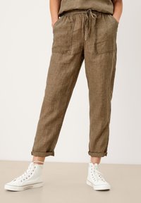 Bruine linnenbroek met een elastische tailleband, een trekkoord en twee voorkanten zakken. Opgerolde manchetten en een gestructureerde afwerking. Gecombineerd met witte hoge sneakers.
