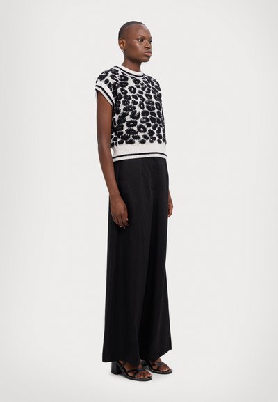 Pulover tricotat cu un model floral în alb și negru, asortat cu pantaloni negri largi și sandale cu toc negre. Design simplu.