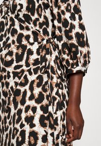 Elokuvamainen leopardi-kuosiset mekko valkoisesta, ruskeasta ja mustasta kankaasta. Mukautettu malli, jossa on sivusiteet ja puffihihat. Liukas pinta.