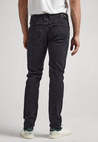 Donkergrijze jeans met een slim-fit, vijf-pocket ontwerp en subtiele stikdetails, gedragen met witte sneakers en een wit T-shirt.