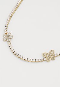 Collier doré mettant en valeur une rangée de cristaux transparents, rehaussé par un design de fleur et de papillon avec des détails décoratifs.