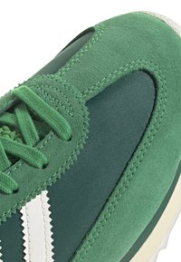Green sneaker featuring a combination of suede and textile materials, textured surface, white zigzag accents, and layered design elements.
