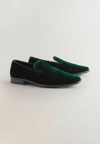 Green velvet slip-on shoes with a sleek design, rounded toe, black accent trim, and textured surface on a flat sole.