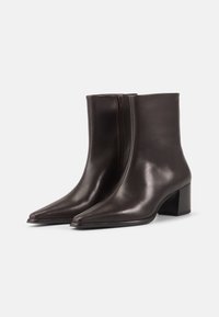 Botines de cuero marrón con diseño de punta afilada, textura suave y una cremallera lateral visible. Cuenta con un tacón mediano para mayor estabilidad.