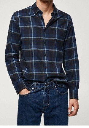 Homme portant une chemise à carreaux bleu foncé et noir à boutons avec un jean bleu foncé, une main dans la poche, recadré au niveau du cou et des cuisses.