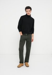 Pull à col roulé noir, pantalon vert olive et baskets beige. Couleurs unies, coupe ajustée avec une texture lisse.