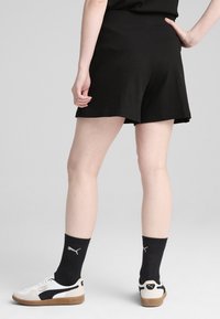 Pantaloni corti neri a costine con vestibilità rilassata, dotati di una cintura liscia e un orlo leggermente svasato, abbinati a sneakers bianche e nere.