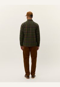 Groen geruit flanellen overhemd met lange mouwen, knoopmanchetten en een bruine corduroy broek. Een bruine baseballpet maakt de outfit compleet.