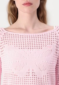 Różowy sweter z dzianiny z dużym wzorem motyla, charakteryzujący się otwartą strukturą splotu i szerokim dekoltem w kształcie łódki. Miękki, lekki materiał.