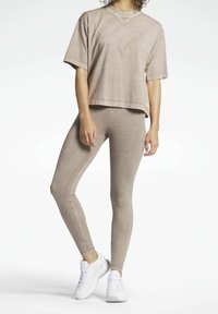 Beżowa bawełniana koszulka typu crop z krótkim rękawem, w połączeniu z dopasowanymi legginsami i białymi trampkami.