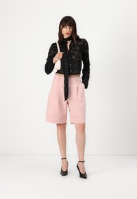 Black lace button-up shirt with floral pattern, paired with pale pink tailored shorts, and black high-heeled shoes. Small pink handbag.
