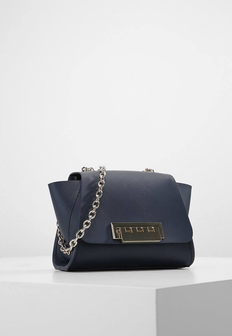 Marinblå läderhandväska med en slät yta, silverkedjespänne och ett rektangulärt spänne i guldton på framsidan. Kort och strukturerad design.