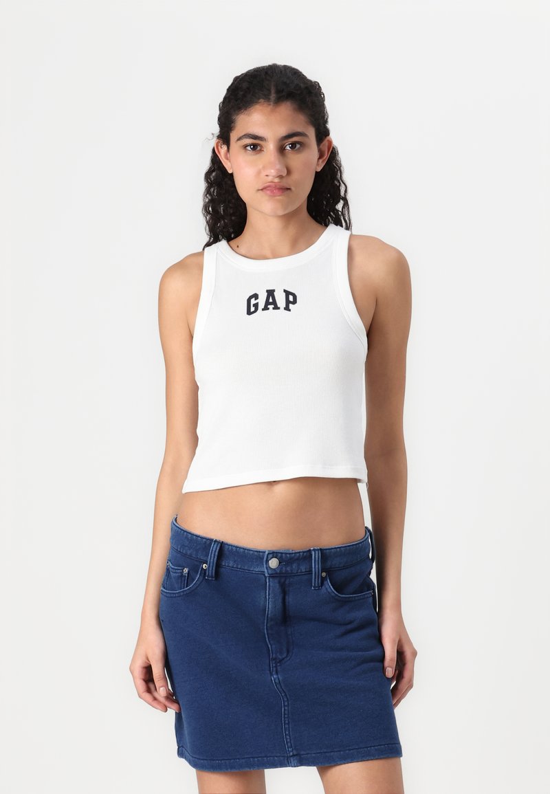 White ribbed crop top featuring "GAP" logo in black, paired with a dark blue denim mini skirt with front pockets and a waist button.