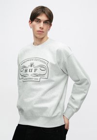 Γκρι φούτερ με στρογγυλή λαιμόκοψη, φέρει κομμένο λογότυπο και κείμενο σε μαύρο χρώμα. Λείος υφαντός, με ριμπ μανίκια και λεπτομέρεια στο τελείωμα.