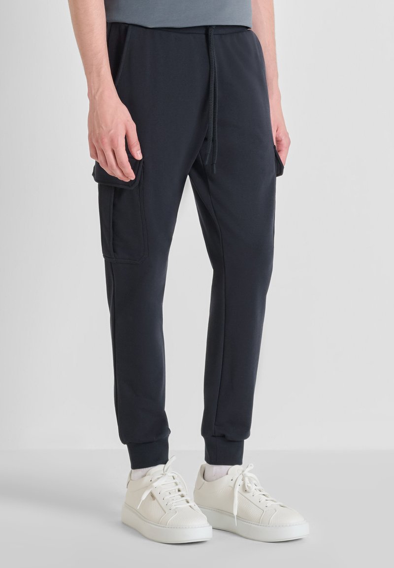 Mornarske jogger hlače od mekanog materijala, s bočnim džepovima, elastičnim manžetama i strukom s vezicom. Nosene s bijelim tenisicama.