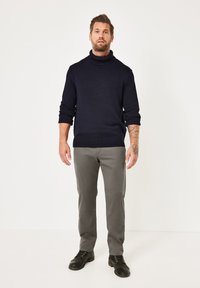 Marinefarbener Rollkragenpullover mit gerippten Bündchen und Saum, kombiniert mit grauen Stoffhosen und schwarzen Schuhen. Das Outfit zeichnet sich durch ein strukturiertes Strickdesign aus.
