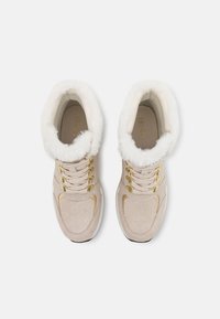 Baskets de sport beiges avec un col en fourrure blanche, accessoires dorés, texture perforée et semelle intérieure rembourrée. Design à lacets avec un bout rond.