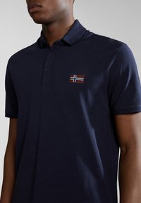 Polo shirt blu navy in una miscela di cotone con patta a tre bottoni e una piccola bandiera norvegese ricamata sul lato sinistro del petto.