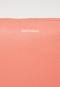 Pink textured leather pouch with a gold zipper and embossed logo "Coccinelle" on the front. Smooth finish, compact design.