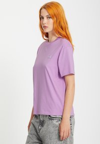 T-shirt en coton lilas clair à col rond et manches courtes. Présente un petit logo sur la poitrine. Coupe décontractée avec une texture lisse.